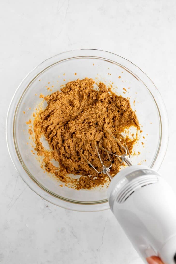 a kitchenaid handheld electric mixer creaming dark brown sugar and vegan butter together