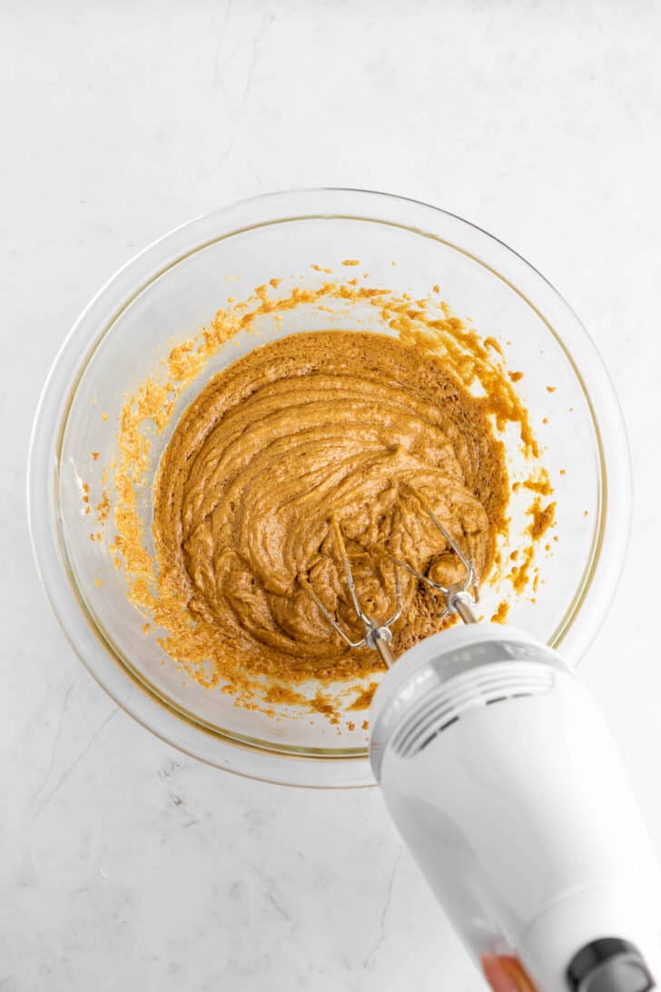 a kitchenaid handheld electric mixer creaming dark brown sugar, molasses, almond milk, and vegan butter together