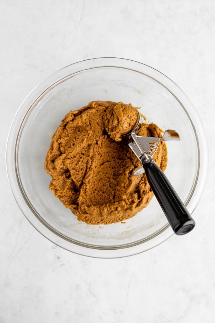 a cookie scoop scooping a ball of vegan brown sugar cookie dough