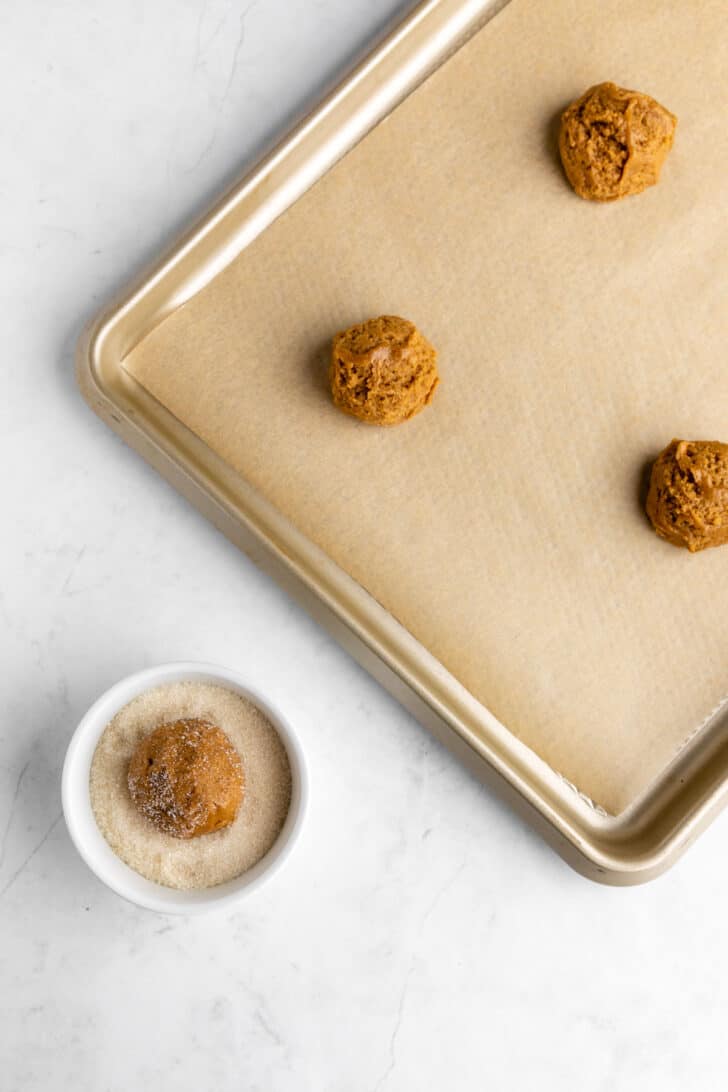rolling balls of vegan brown sugar cookie dough in granulated sugar