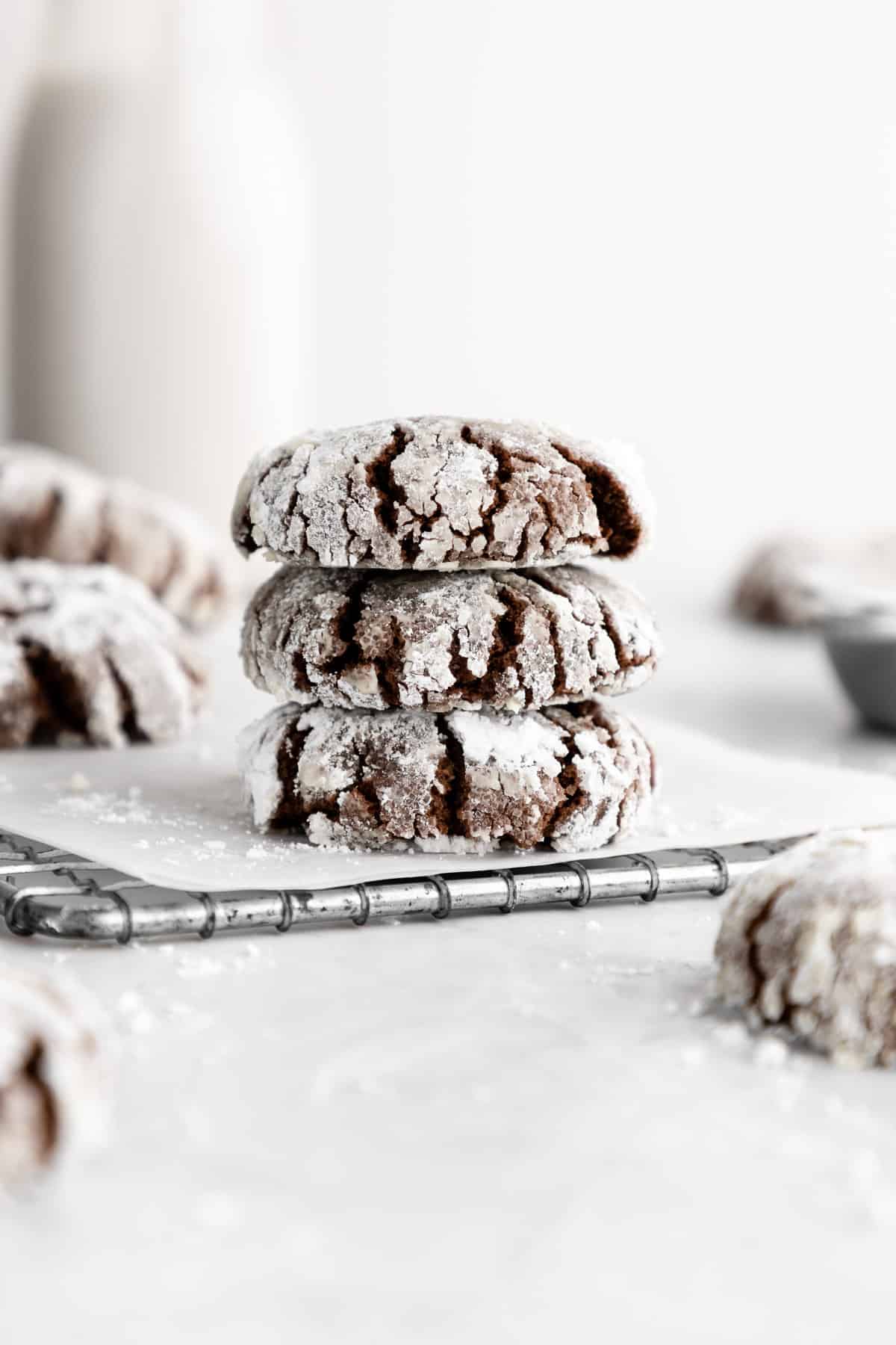 a stack of vegan chocolate crinkle cookies with powdered sugar on a wire cooling rack