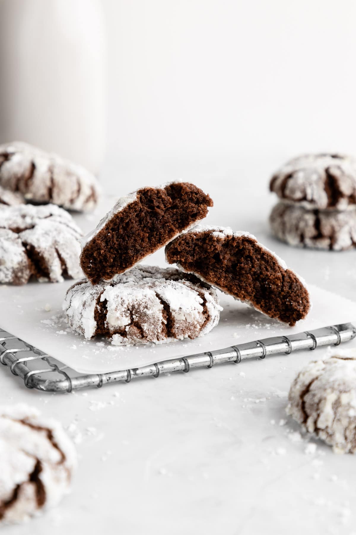 a pile of vegan chocolate crinkle cookies with powdered sugar on a wire cooling rack