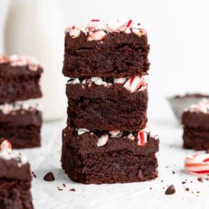 a stack of three vegan peppermint brownies with crushed candy canes and chocolate ganache