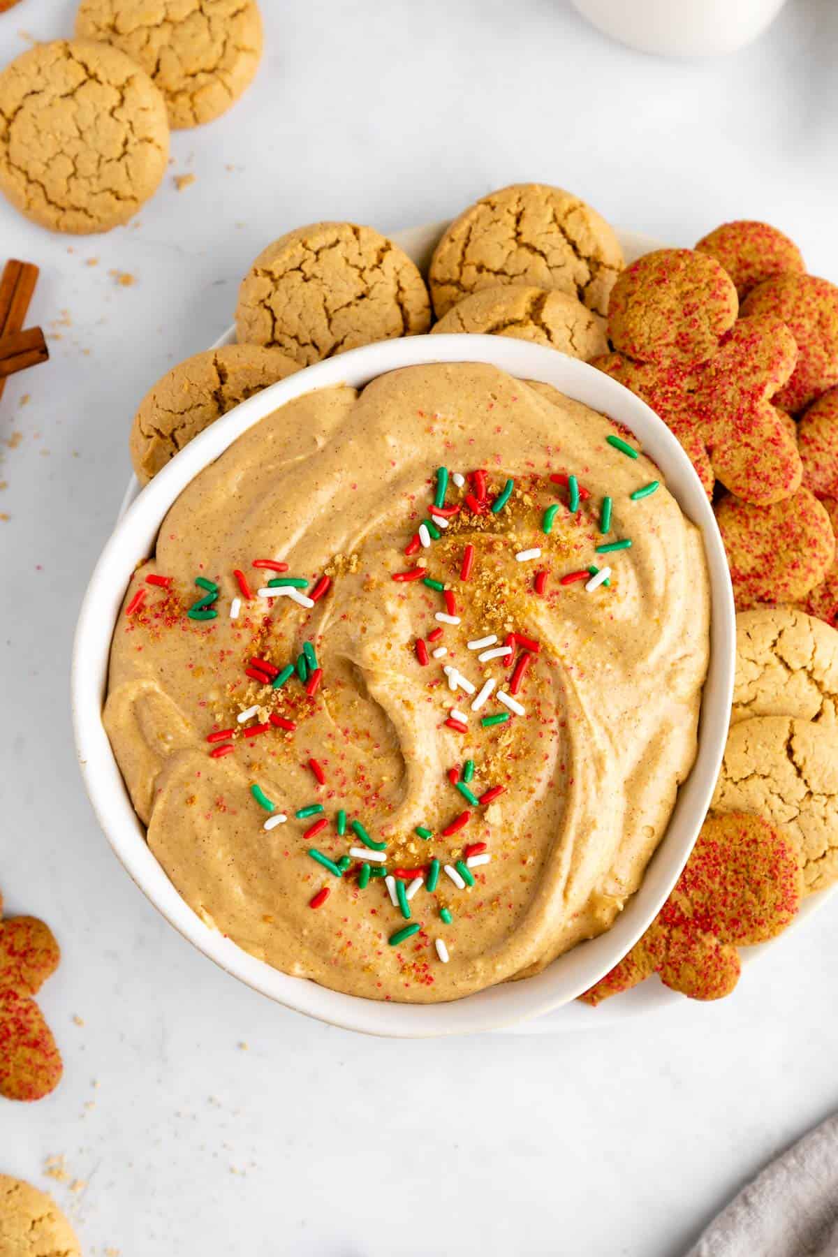 vegan gingerbread cookie dip in a bowl with sprinkles and a plate of holiday cookies