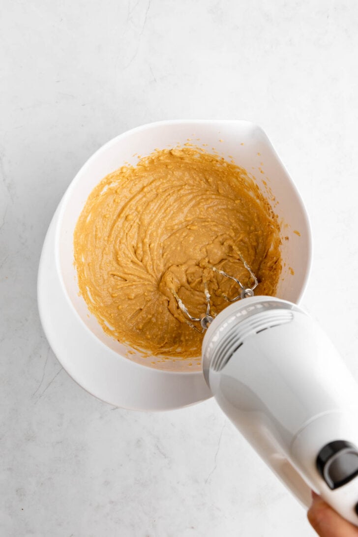 an electric handheld mixer creaming together vegan gingerbread cookie dip in a white bowl
