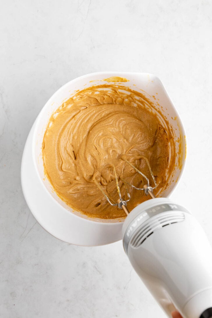 a handheld mixer creaming together vegan gingerbread cookie dip in a white bowl