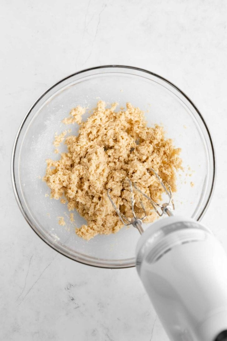 a handheld mixer creaming together vegan butter and sugar in a glass mixing bowl