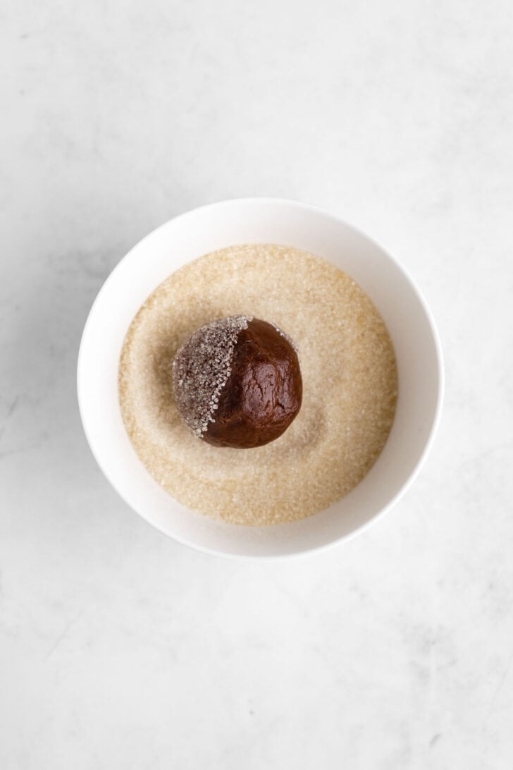 rolling a ball of vegan chocolate cookie dough in a bowl of granulated sugar