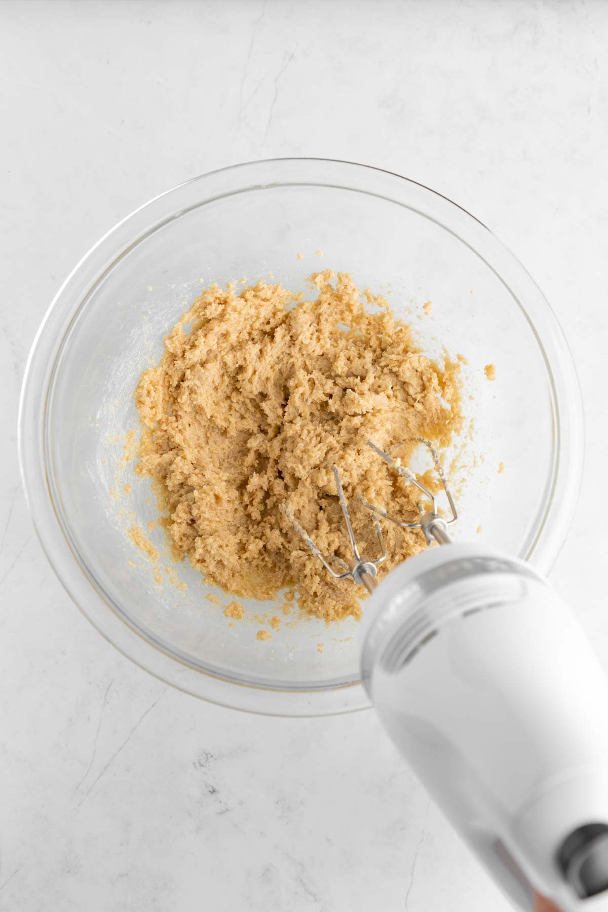 a handheld mixer creaming vegan butter and sugar together in a glass mixing bowl