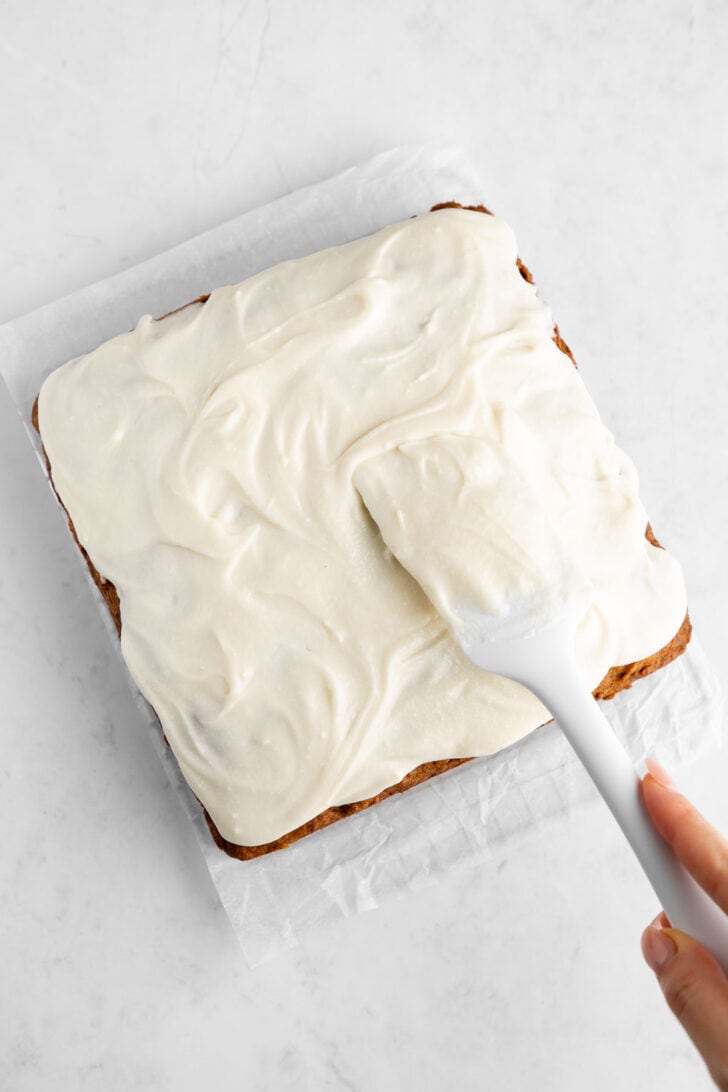 a silicone spatula spreading dairy-free cream cheese frosting on a vegan pumpkin cake