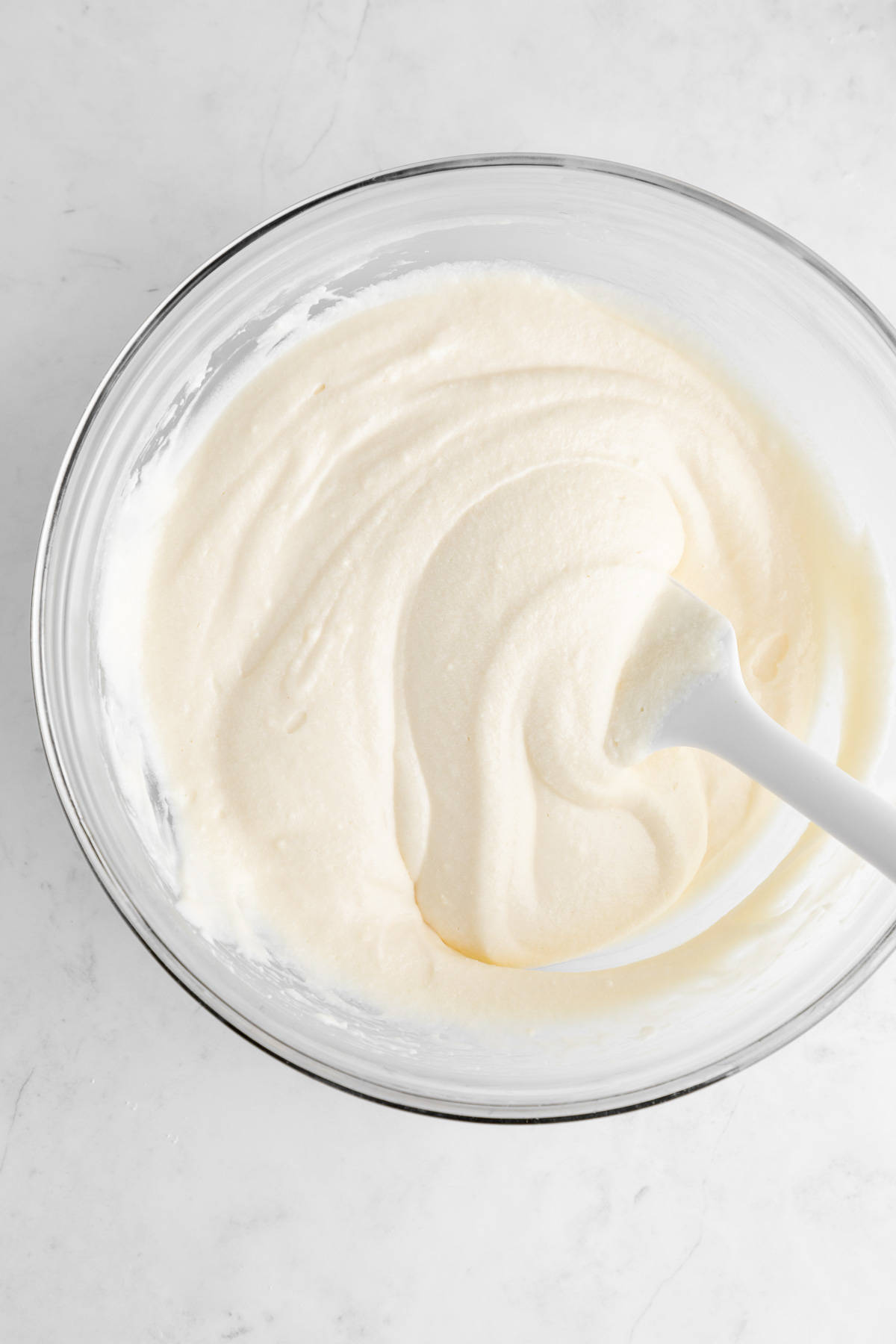 a silicone spatula mixing vegan cream cheese frosting in a glass mixing bowl