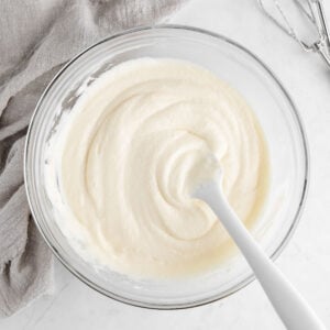 a silicone spatula mixing dairy-free cream cheese frosting in a glass mixing bowl