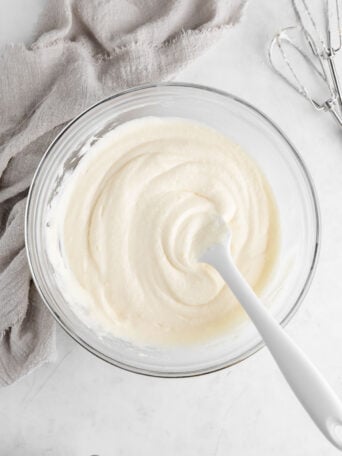 a silicone spatula mixing dairy-free cream cheese frosting in a glass mixing bowl