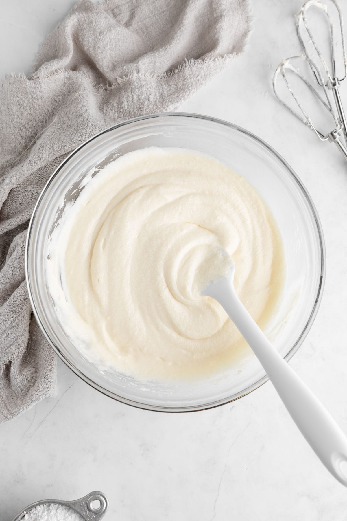 a silicone spatula mixing dairy-free cream cheese frosting in a glass mixing bowl