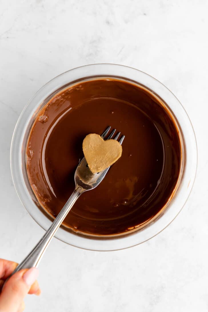 a fork dipping a sunbutter heart into melted chocolate