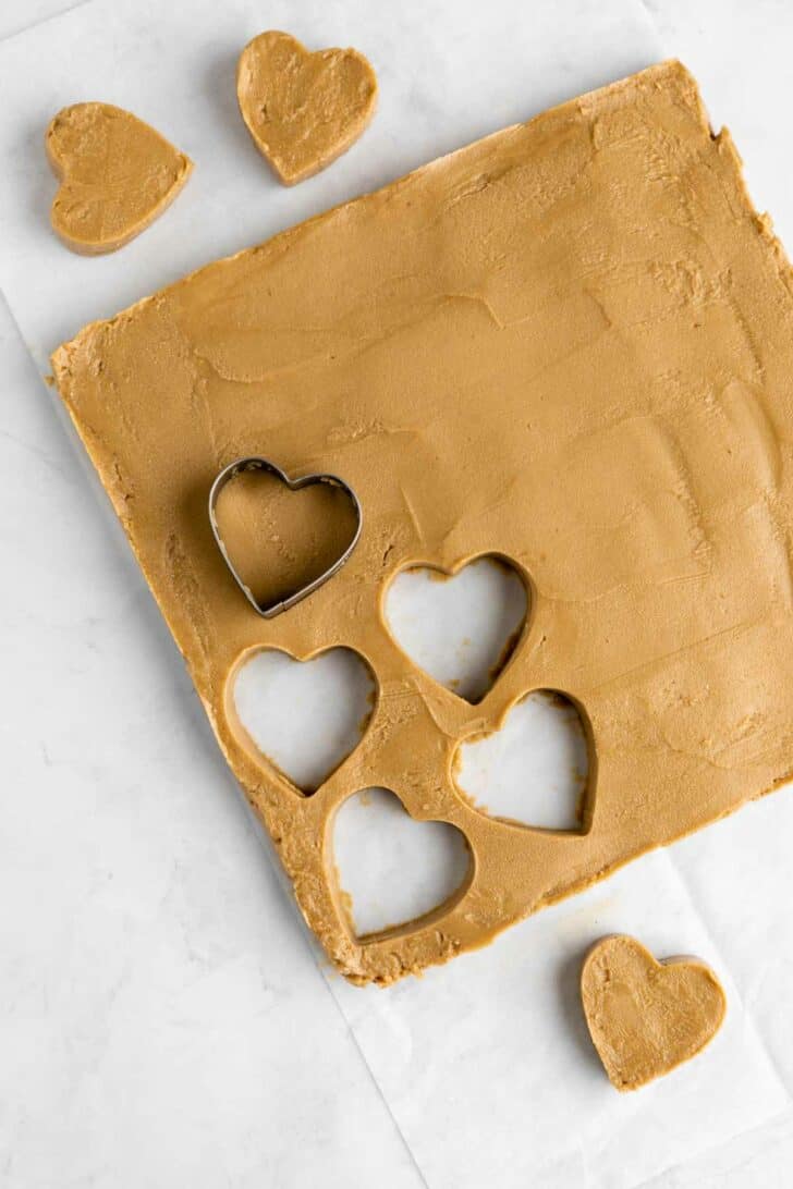 a heart shaped cookie cutter slicing hearts out of sunflower butter dough