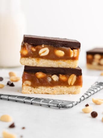 a stack of two vegan snickers cookie bars with caramel and peanuts