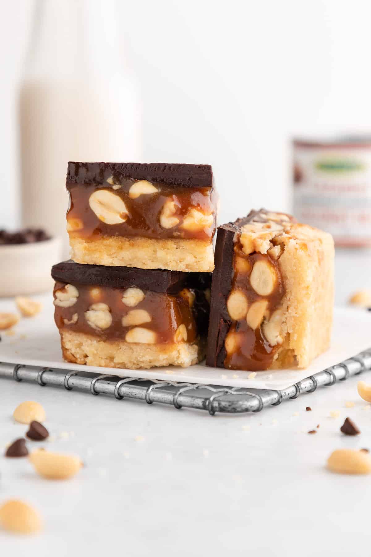 a pile of three vegan snickers cookie bars with caramel and peanuts