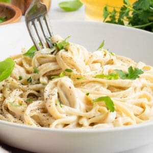 a fork twirling vegan fettuccine alfredo pasta in a white bowl