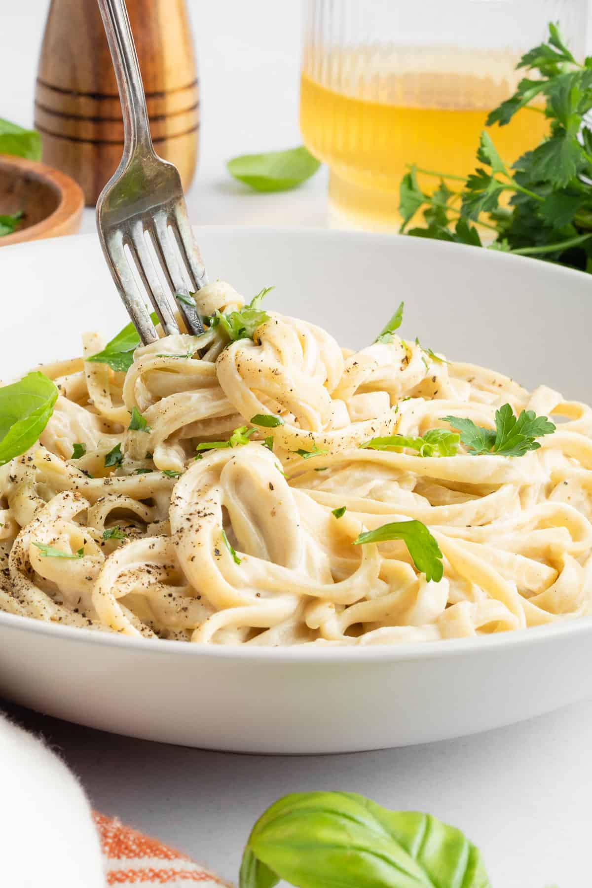 a fork twirling vegan fettuccine alfredo pasta in a white bowl