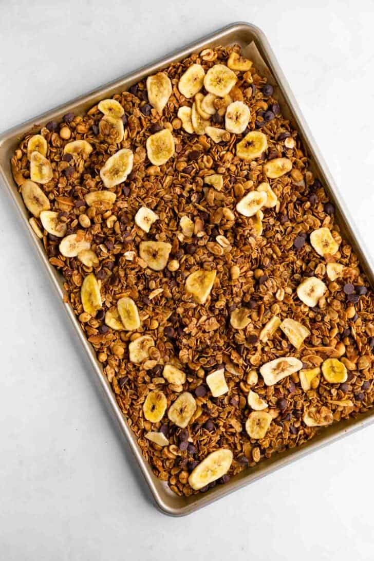 homemade chunky monkey granola with banana chips, chocolate chips, nuts, and coconut on a baking sheet