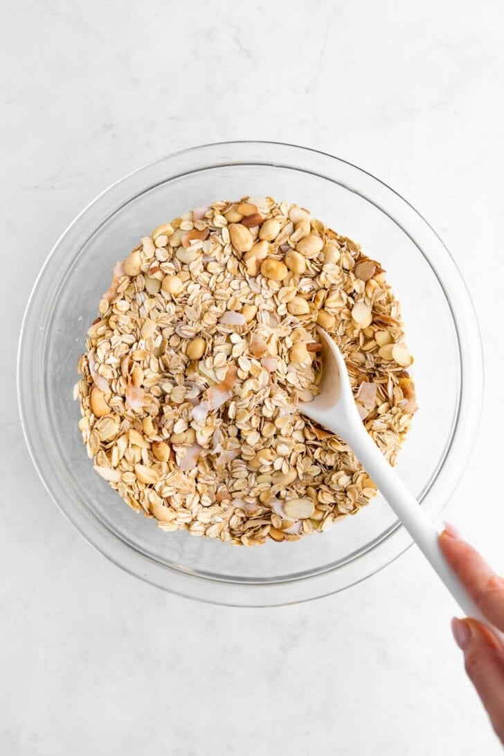 mixing chunky monkey granola ingredients in a glass bowl