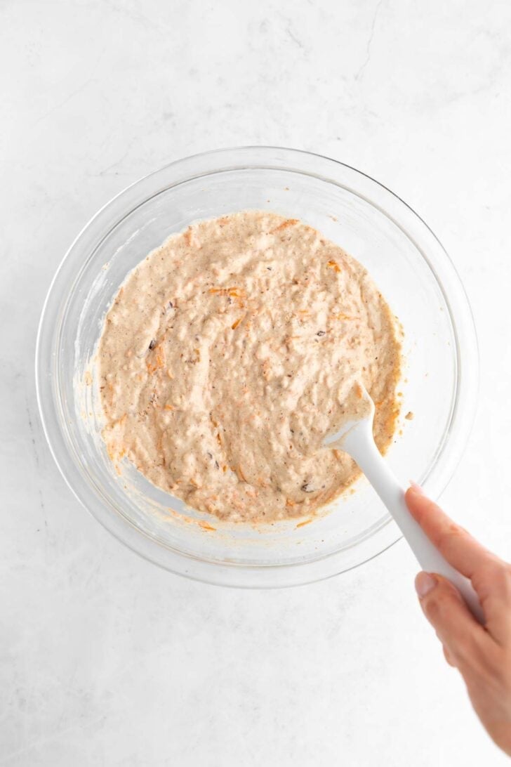 a hand mixing vegan carrot cake pancake batter in a glass bowl