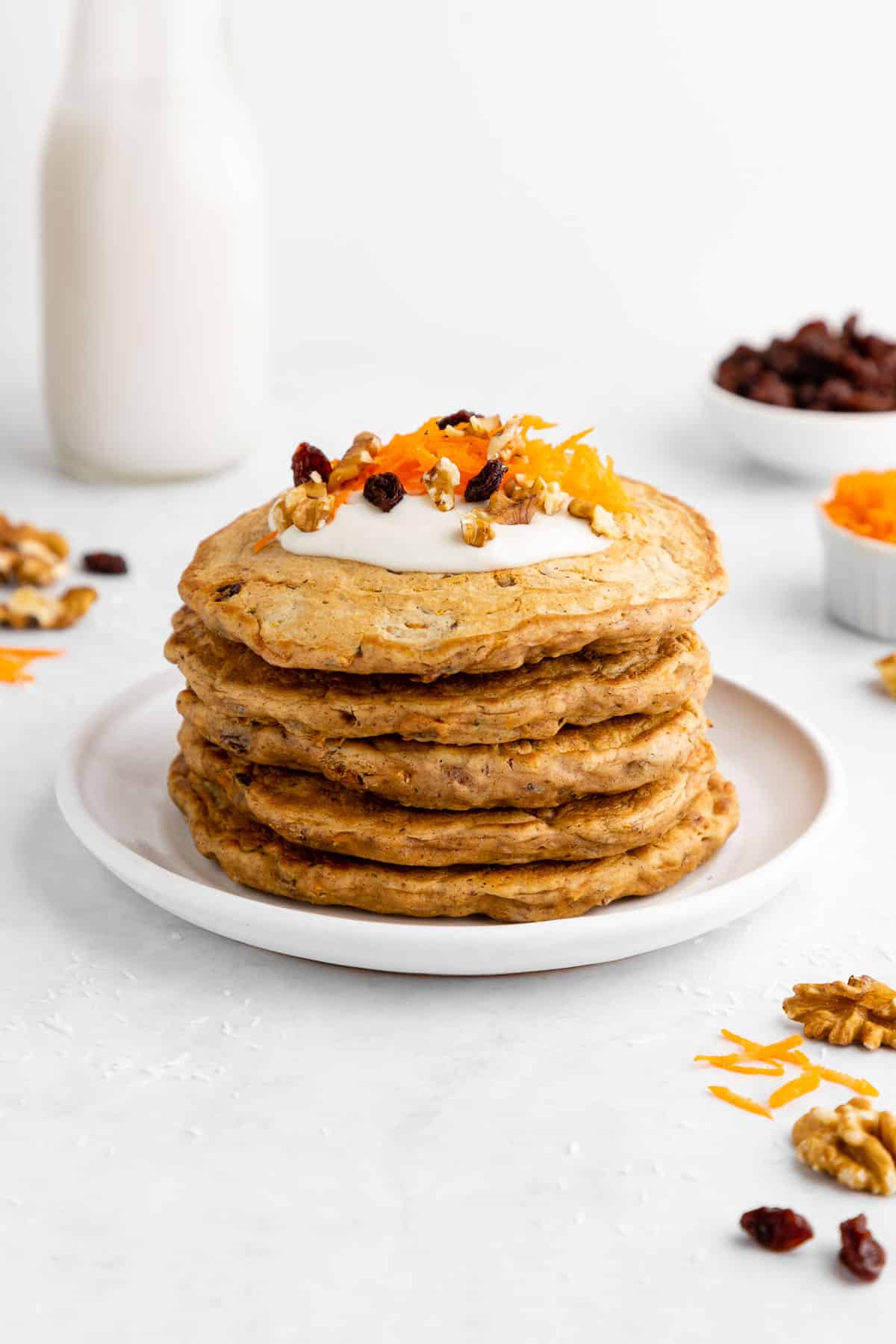 a stack of vegan carrot cake pancakes with cream cheese icing, raisins, and walnuts