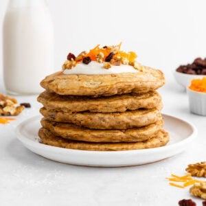 a stack of vegan carrot cake pancakes with cream cheese icing, raisins, and walnuts