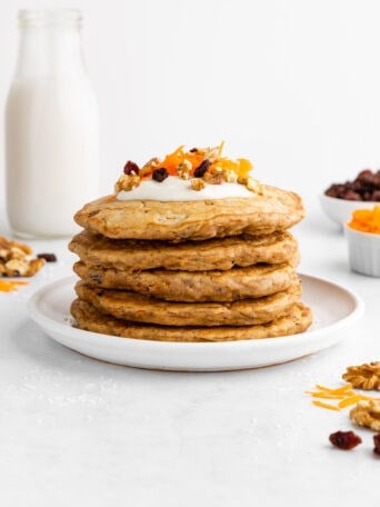 a stack of vegan carrot cake pancakes with cream cheese icing, raisins, and walnuts