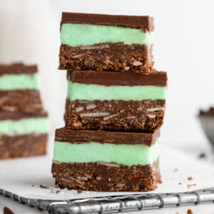 a stack of three vegan mint nanaimo bars with mint buttercream frosting and chocolate ganache