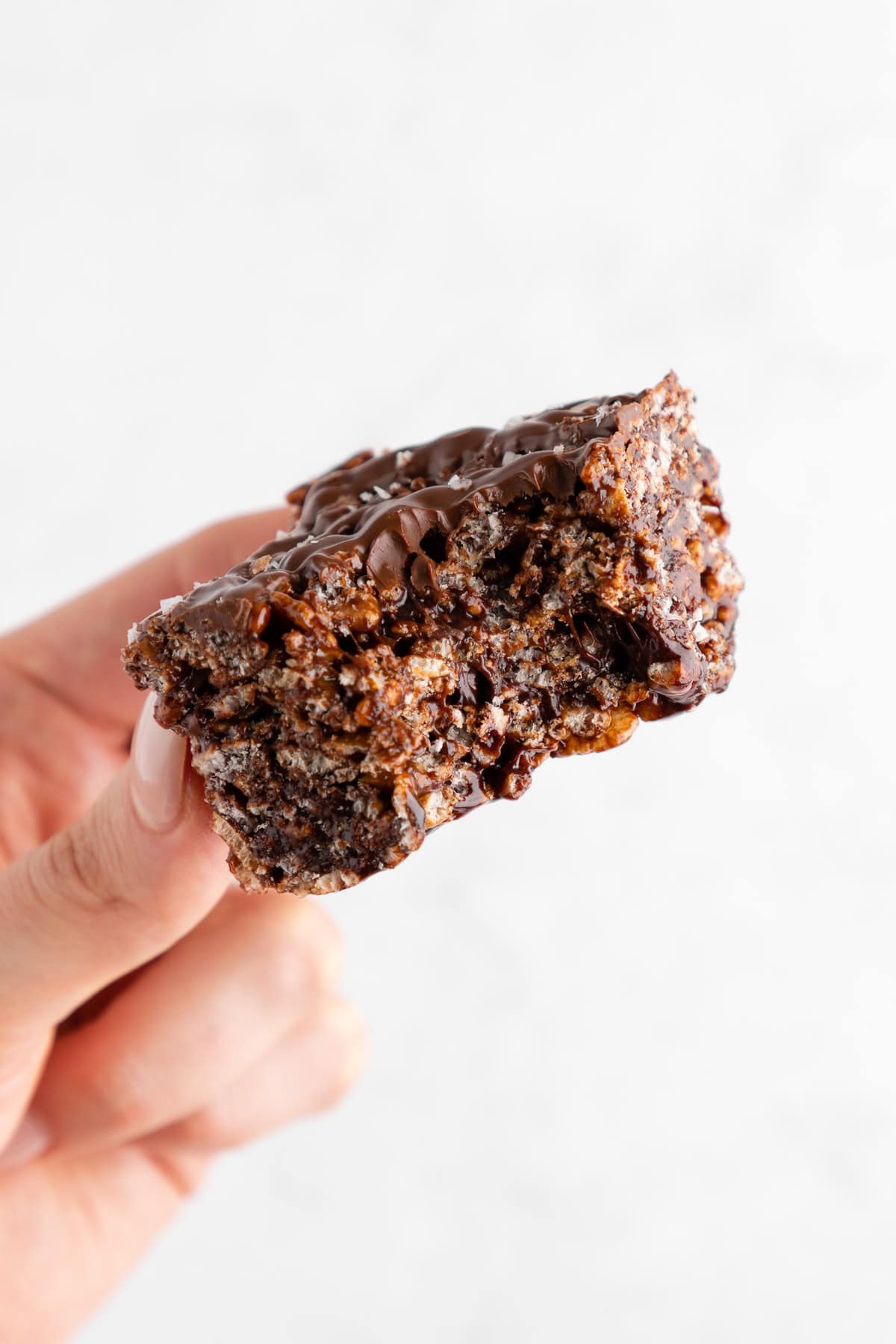 a hand holding a a stack of two vegan chocolate rice krispie treat with a bite taken out of it
