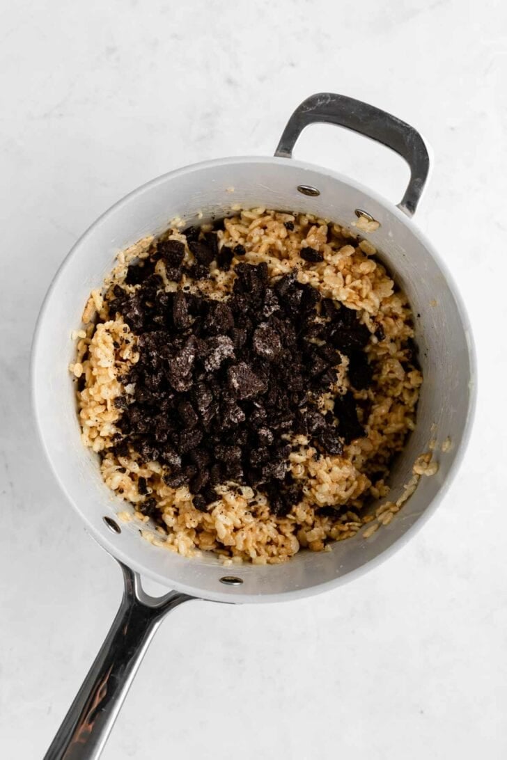 mixing crushed oreos into rice krispie treats inside a pot