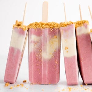 a pile of vegan strawberry cheesecake popsicles with graham cracker crumbs
