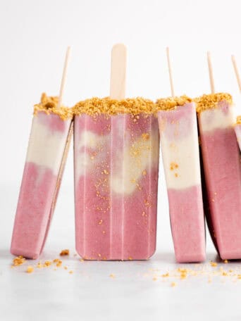 a pile of vegan strawberry cheesecake popsicles with graham cracker crumbs