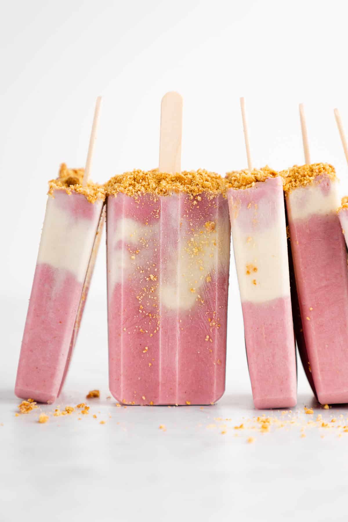 a pile of vegan strawberry cheesecake popsicles with graham cracker crumbs
