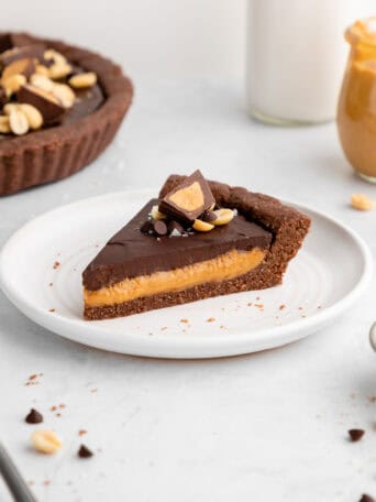 a slice of healthy no-bake chocolate peanut butter tart on a white plate with peanut butter cups