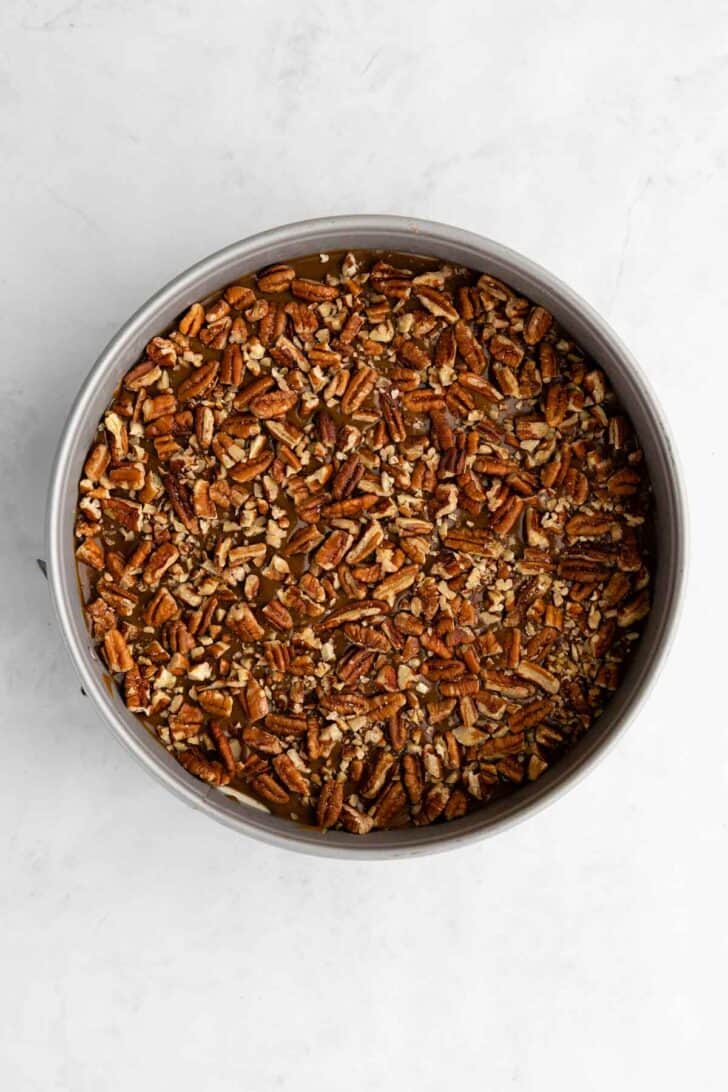 crushed pecans and vegan caramel sauce spread over no-bake cheesecake inside a cake pan