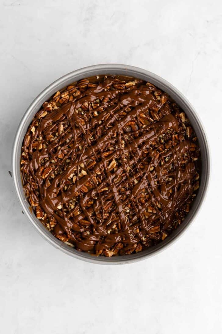 melted chocolate, crushed pecans, and vegan caramel sauce spread over no-bake cheesecake inside a cake pan