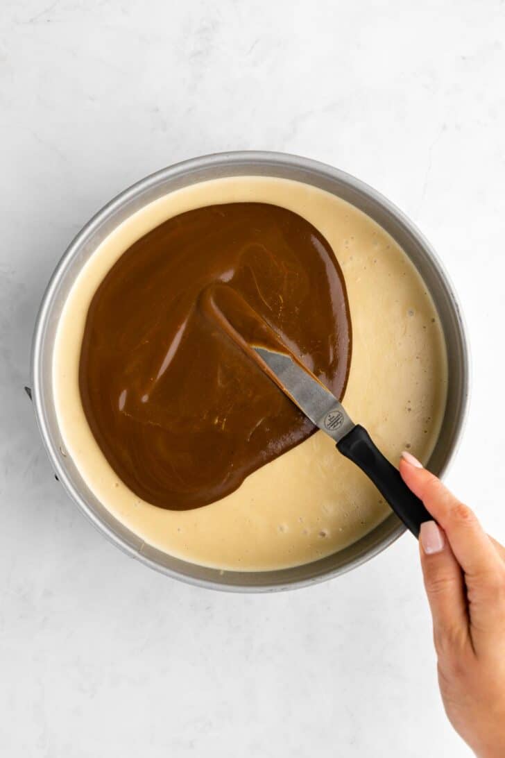 spreading vegan caramel sauce over no-bake cheesecake inside a cake pan