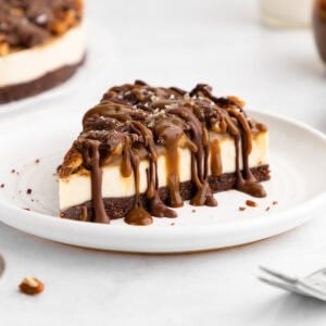 a slice of no-bake turtle cheesecake with caramel sauce, pecans, and chocolate on a plate