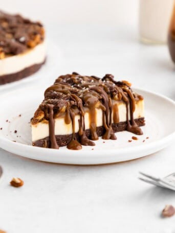 a slice of no-bake turtle cheesecake with caramel sauce, pecans, and chocolate on a plate