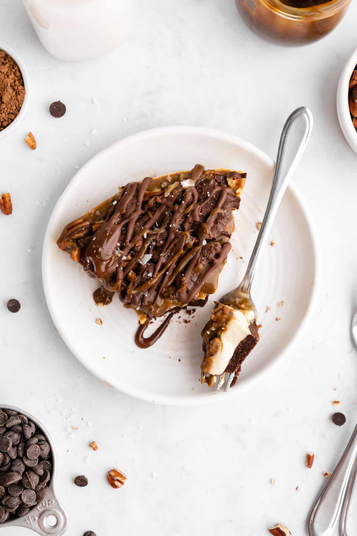 a slice of no-bake turtle cheesecake with caramel sauce, pecans, and chocolate on a plate with a fork