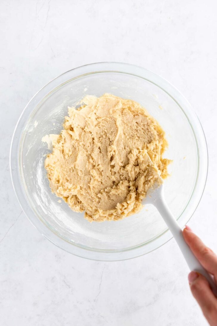a rubber spatula mixing birthday cake cookie dough in a glass bowl