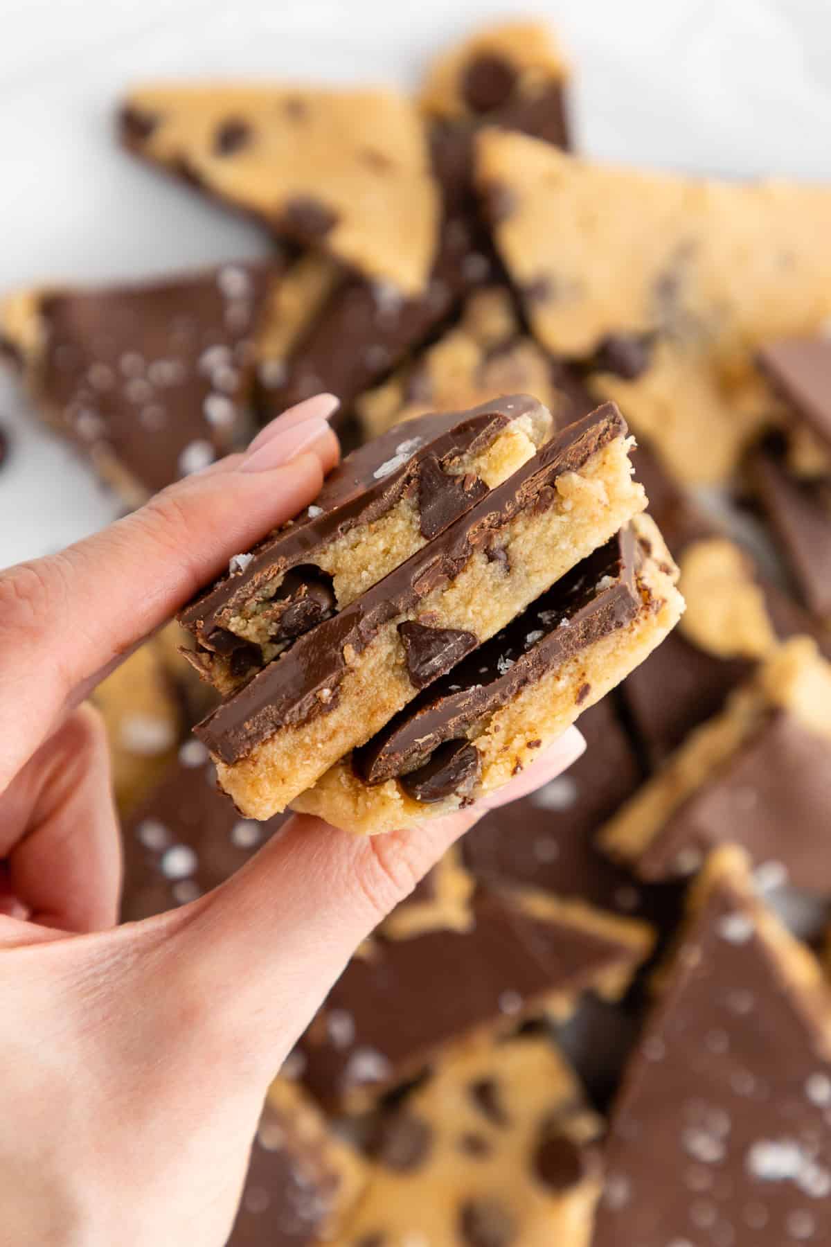 a hand holding three pieces of almond flour healthy cookie dough bark