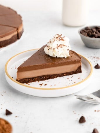 a slice of no-bake chocolate cheesecake with vegan chocolate ganache and whipped cream on a ceramic plate