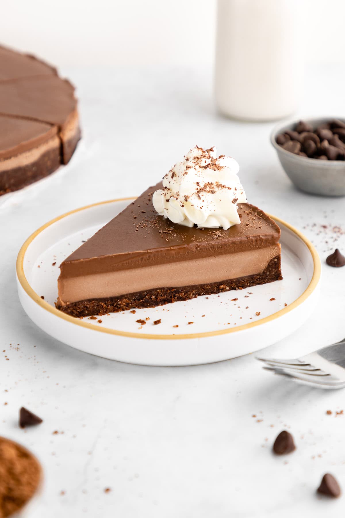 a slice of no-bake chocolate cheesecake with vegan chocolate ganache and whipped cream on a ceramic plate