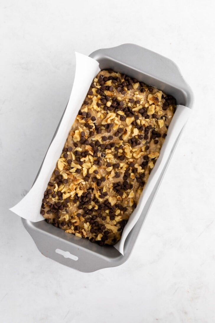 vegan banana bread batter with chocolate chips and walnuts inside a loaf pan
