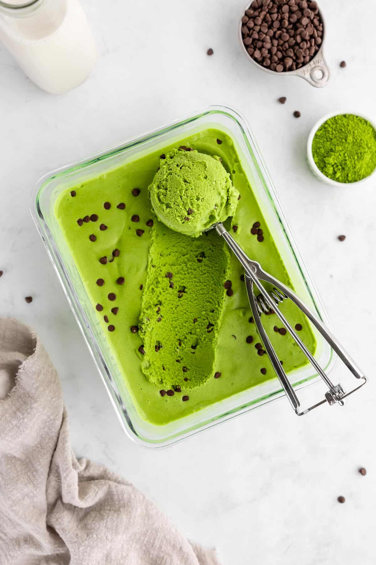 scooping chocolate chip vegan matcha ice cream out of a glass container