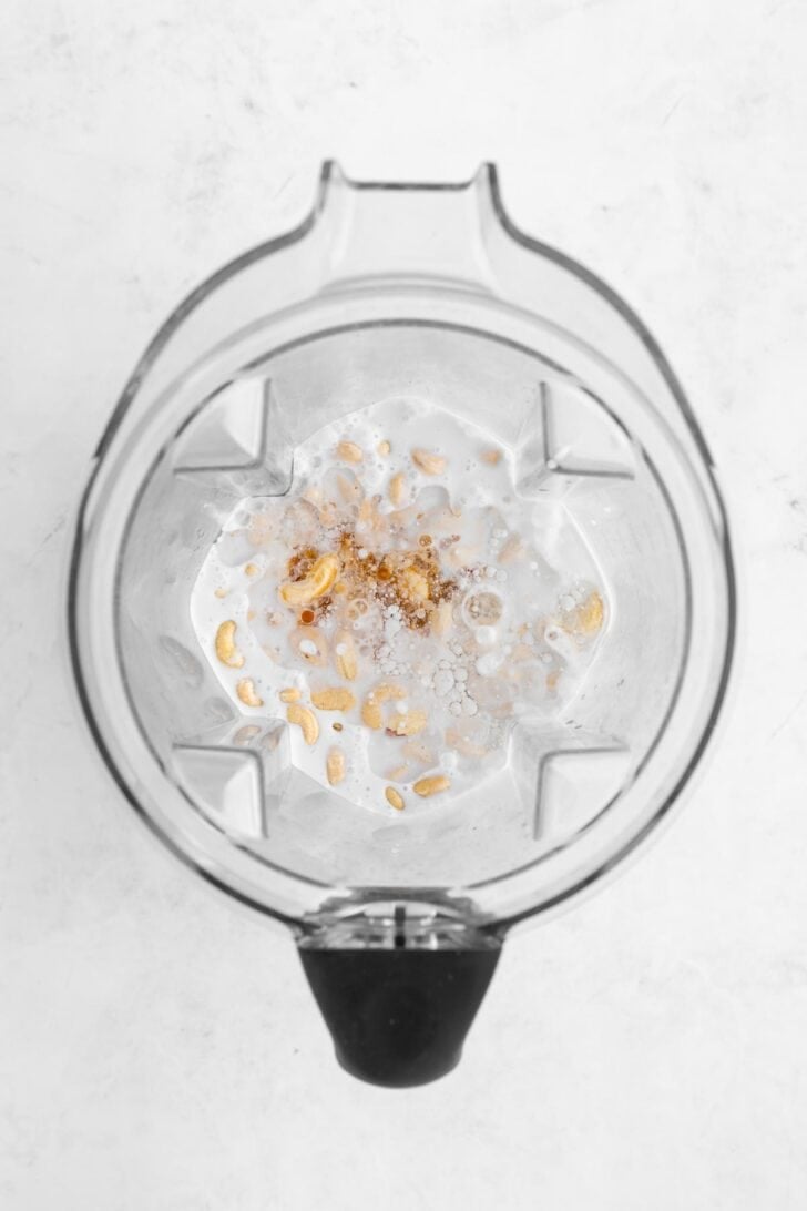raw cashews, coconut milk, coconut oil, and maple syrup inside a Vitamix blender